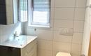 Ein modernes Badezimmer mit großen Fliesen und einem schlichten Design. Es verfügt über ein Waschbecken, einen Spiegel und eine Toilette.
