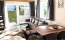 Eine helle und moderne Wohnküche mit einem gemütlichen Sofa und einem Esstisch. Große Fenster lassen viel Tageslicht herein und bieten Blick auf einen gepflegten Garten.