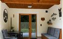 A cozy terrace with wooden beams and a large window. There is a table with chairs and a wooden bench.