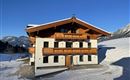 A modern chalet in alpine style, surrounded by snow. The clear blue sky complements the picturesque landscape.