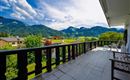 A beautiful balcony overlooking the green mountains and the blue sky. In the foreground, there are chairs, and the surroundings are lush and inviting.