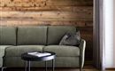 A modern living room with a comfortable, gray-green sofa and a small black table. The wooden wall combined with curtains creates a cozy atmosphere.