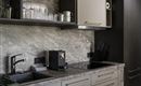 A modern kitchen with an elegant countertop and minimalist furniture. There are glasses, mugs, and a coffee machine on the countertop.