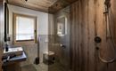 A modern bathroom with wooden paneling and gray tiles. It includes a glass shower, a sink, and a small window.