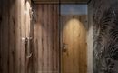 A modern shower with wood paneling and a glass partition. In the background, a door with a simple design is visible.