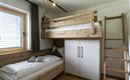A modern bedroom with a wooden bunk bed and a single bed. The walls are light and there is a large window with a view of the surroundings.