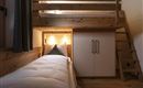A cozy bedroom with a loft bed and a single bed side. The room is made of wood and features a modern wardrobe.