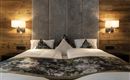 A stylish bedroom with two beds and a cozy wooden paneling. An elegant headboard and decorative pillows complete the ambiance.