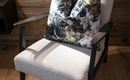 A comfortable armchair with a colorful cushion stands in front of a wooden wall. The room has a warm and inviting atmosphere.
