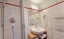 A modern bathroom with a shower and sink. The walls are tiled and there is a towel warmer.
