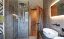 A modern bathroom with a glass shower and sink. The walls are in neutral gray tones, and wooden details create a warm atmosphere.