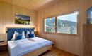 A cozy bedroom with wooden paneling and large windows. You have a beautiful view of the mountains.