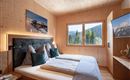 A modern bedroom with bright wood decor and large windows. The room is cozily furnished and offers a view of the surrounding mountains.