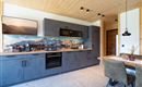 A modern kitchen with gray cabinets and a wooden ceiling. A dining table with chairs is next to the kitchen unit.