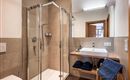 A modern bathroom with a glass shower and a stylish sink. Towels are neatly placed on a wooden shelf.