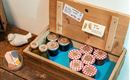 A wooden box with various jars and jam with checkered lids. It also contains small signs with prices.