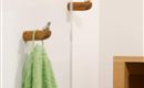Een minimalistisch badkamergebied met een groene handdoek die aan een houten houder hangt. Op de achtergrond is een glazen wand en een wandplank zichtbaar.