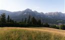 Een schilderachtig landschap met groene weilanden en majestueuze bergen op de achtergrond. De lucht is helder en de sfeer is vredig.
