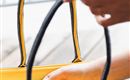 Een hand grijpt naar een sleutelhanger in een tas. De tas heeft een oranje binnenzijde en zwarte hengsels.