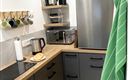 Een moderne keuken met een houten werkblad, een koelkast en een magnetron. Keukenbenodigdheden en kopjes hangen netjes aan de muur.
