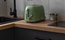 Een moderne toaster in een minimalistische keukenomgeving. De combinatie van een groene toaster, een houten werkblad en donkere kasten creëert een uitnodigende sfeer.