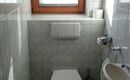 A small bathroom with white tiles and a window. There is a toilet and a sink.
