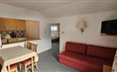 A cozy living room with a red sofa and a dining table. The open kitchen is well-equipped and has wooden cabinets.