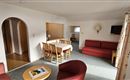 A bright living room with a red sofa and a dining table. The atmosphere is cozy and inviting.