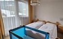 A bright bedroom with two beds and a crib. Large windows let in a lot of light.