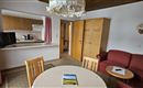 A cozy apartment with an open kitchen and a dining area. The room features a red sofa and a table with chairs.
