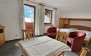 A cozy room with a double bed, two red chairs, and a table. Large windows offer a view of the mountains outside.