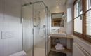 A modern bathroom with a glass shower and a wooden sink. The windows let in plenty of daylight.