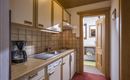 A small kitchen with light wooden cabinets and modern amenities. The space is tidy and inviting with access to another room.
