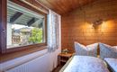 A cozy bedroom with wooden paneling and a window overlooking a green view. The beds are invitingly decorated with white pillows and blankets.