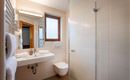 Ein modernes Badezimmer mit Dusche, Waschbecken und Spiegel. Helle Fliesen und natürliche Beleuchtung durch ein Fenster sorgen für eine freundliche Atmosphäre.