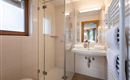 Ein modernes Badezimmer mit einer Glasdusche und einem Waschbecken. Helle Fliesen und ein großer Spiegel sorgen für eine freundliche Atmosphäre.