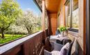 Ein gemütlicher Balkon mit Blick auf einen blühenden Garten. Ein Tisch mit Blumen und zwei Stühlen lädt zum Entspannen ein.