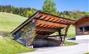 Eine moderne Garage aus Holz mit einem schrägen Dach steht in einer grünen Landschaft. Im Hintergrund sind sanfte Hügel und Bäume zu sehen.