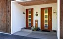 Der Eingang zu einem modernen Haus mit zwei Holztüren. Neben den Türen steht eine dekorierte Pflanze auf der Veranda.