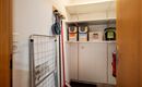 Ein kleiner Abstellraum mit Regalen und verschiedenen Aufbewahrungsboxen. An der Wand hängen Reinigungsutensilien und eine Garderobe.