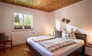 Ein helles Schlafzimmer mit einem Doppelbett und karierten Kissen. Neben dem Bett steht ein Stuhl und ein Fenster lässt natürliches Licht herein.