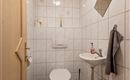 A small, clean bathroom with white tiles. It includes a toilet, a sink, and a towel rack.