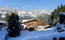 Ein idyllisches Chalet in einer schneebedeckten Landschaft. Im Hintergrund sind beeindruckende Berggipfel zu sehen.