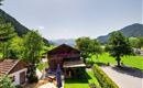 A picturesque landscape with a traditional wooden house and green meadows. In the background, gentle mountains and a clear sky can be seen.