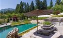 Ruhiger Gartenbereich des Hotel Alpenpanorama mit Sonnenliegen, Sonnenschirm und Naturpool im Hintergrund.