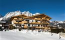 Ein modernes Chalet im Schnee mit Blick auf die Berge. Der klare blaue Himmel ergänzt die winterliche Landschaft.
