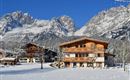 A picturesque winter village with snow-covered mountains in the background. The traditional wooden houses are surrounded by an idyllic snowy landscape.