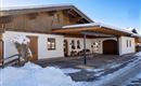 A modern house in the snow with wood siding and garage space. The surroundings are wintry and inviting.
