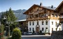 Een traditioneel houten huis in de Alpen met meerdere balkons. Omringd door bomen en een prachtig berglandschap.