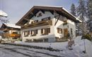 A traditional house in the snow with a balcony and wooden windows. The surroundings are wintry and peaceful.
